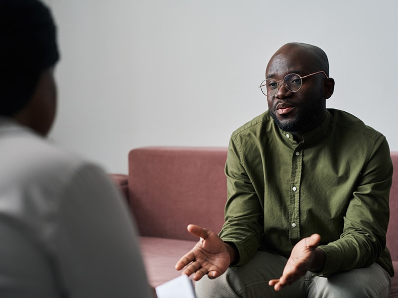 Young man in casualwear sitting on couch and explaining his emotions and worries during talk with psychoanalyst
